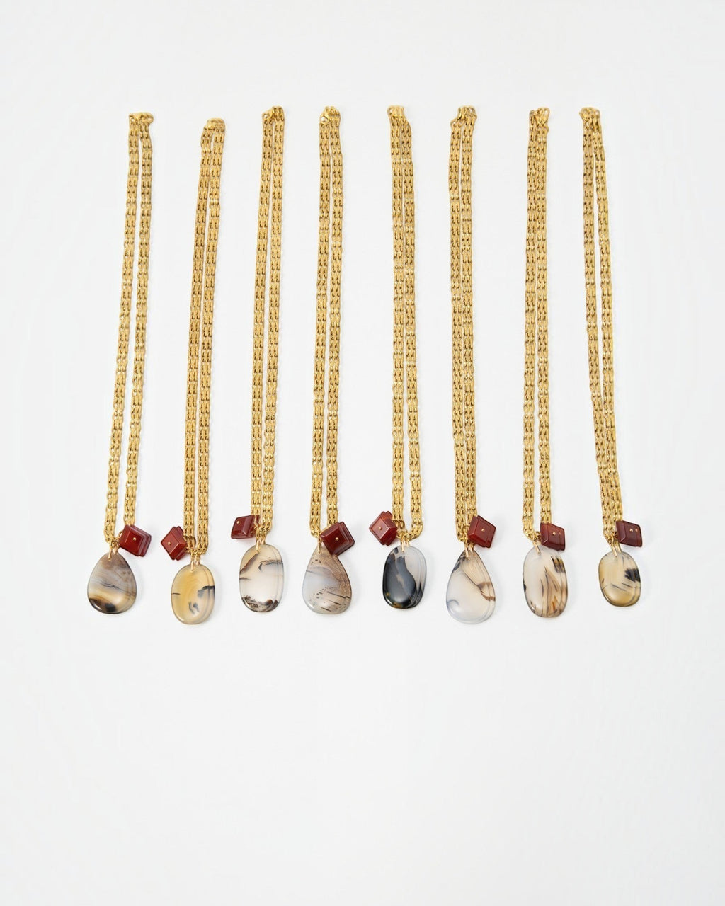 Elsita Jewelry Calligraphy necklaces featuring teardrop-shaped agate pendants and small red beads on gold chains.