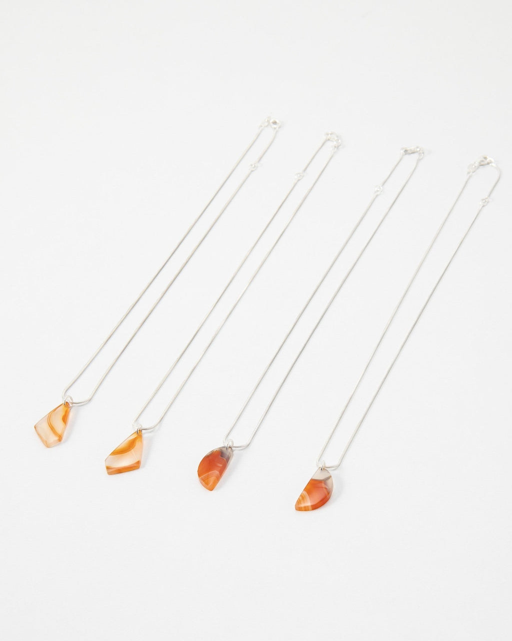 Four Elsita Jewelry Citrus II necklaces featuring polished orange agate pendants on delicate silver chains.
