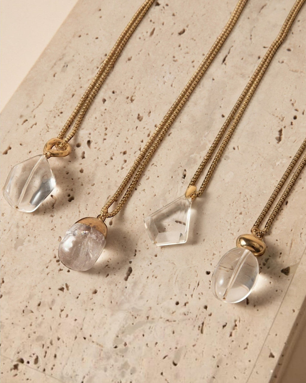 Elsita Jewelry Lustre I collection featuring four unique clear quartz pendants on gold-tone stainless steel chains.