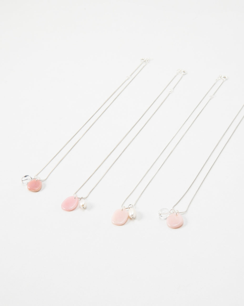 Four Elsita Jewelry Petal Clear necklaces featuring delicate silver chains with pink petal charms and pearl accents.