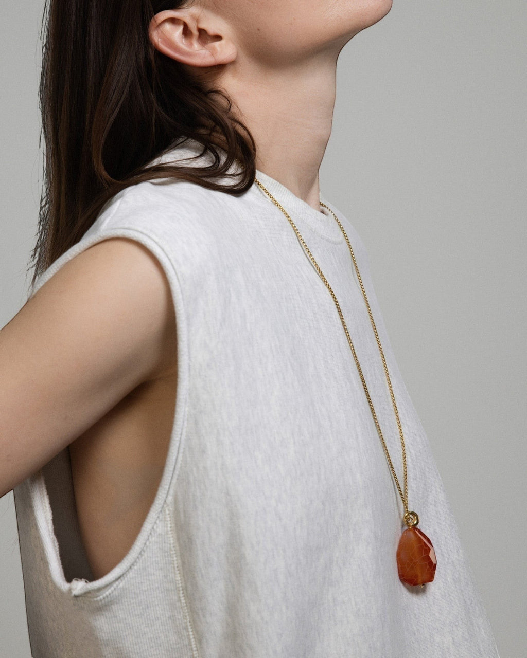 Model wearing an Elsita Jewelry Sechseläuten necklace featuring a large fire agate and white agate pendant on a gold chain.