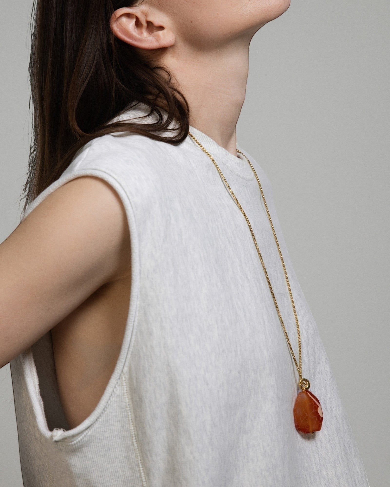 Model wearing an Elsita Jewelry Sechseläuten necklace featuring a large fire agate and white agate pendant on a gold chain.